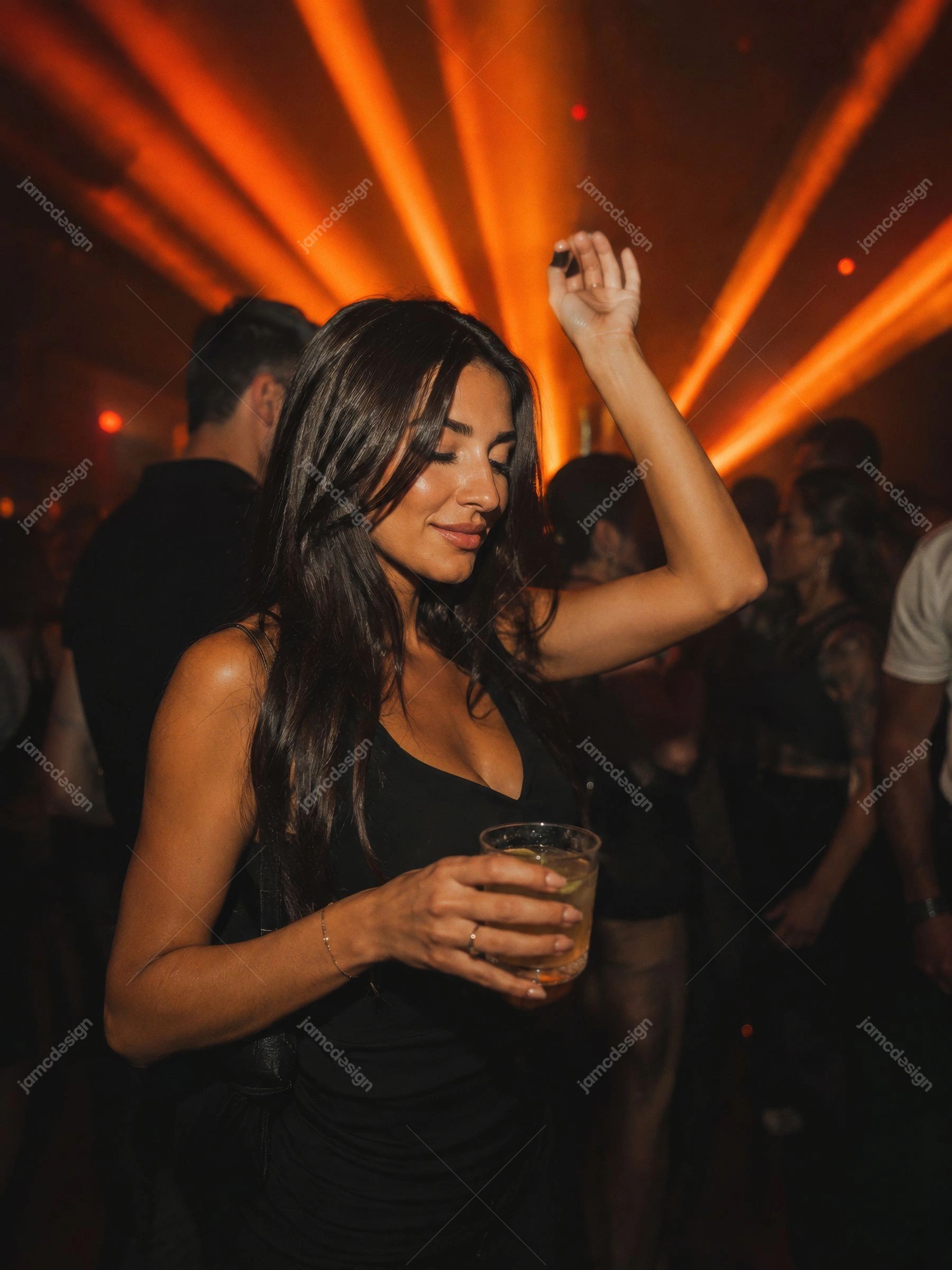 Woman Dancing With Drink Under Orange Lasers Club Glow Portrait. JPG photo of a woman dancing with a drink in a dark nightclub