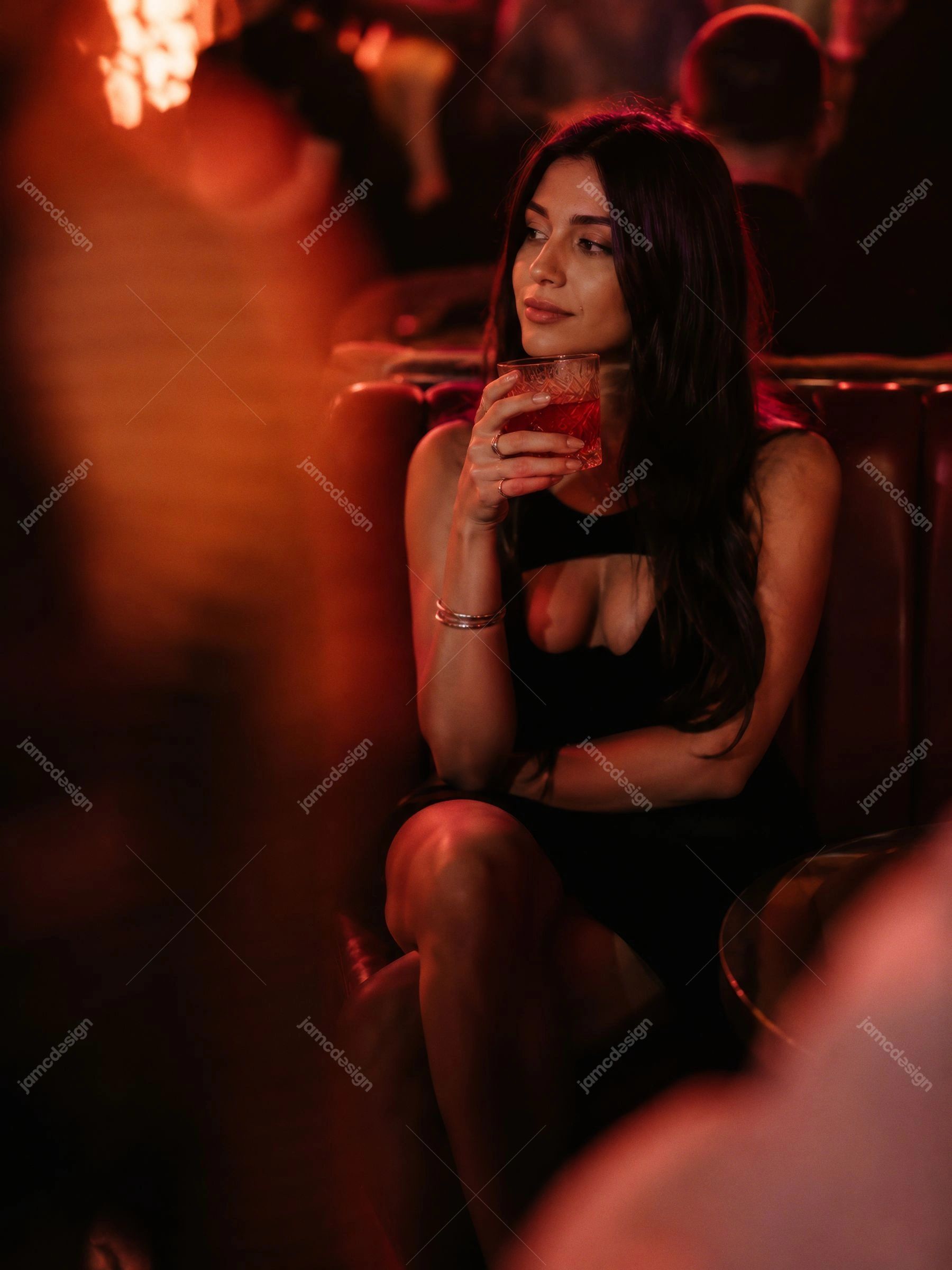 Woman Relaxing With Cocktail In Luxury Nightclub Lounge. This JPG photo shows a seated woman holding a cocktail glass in a dark nightclub lounge