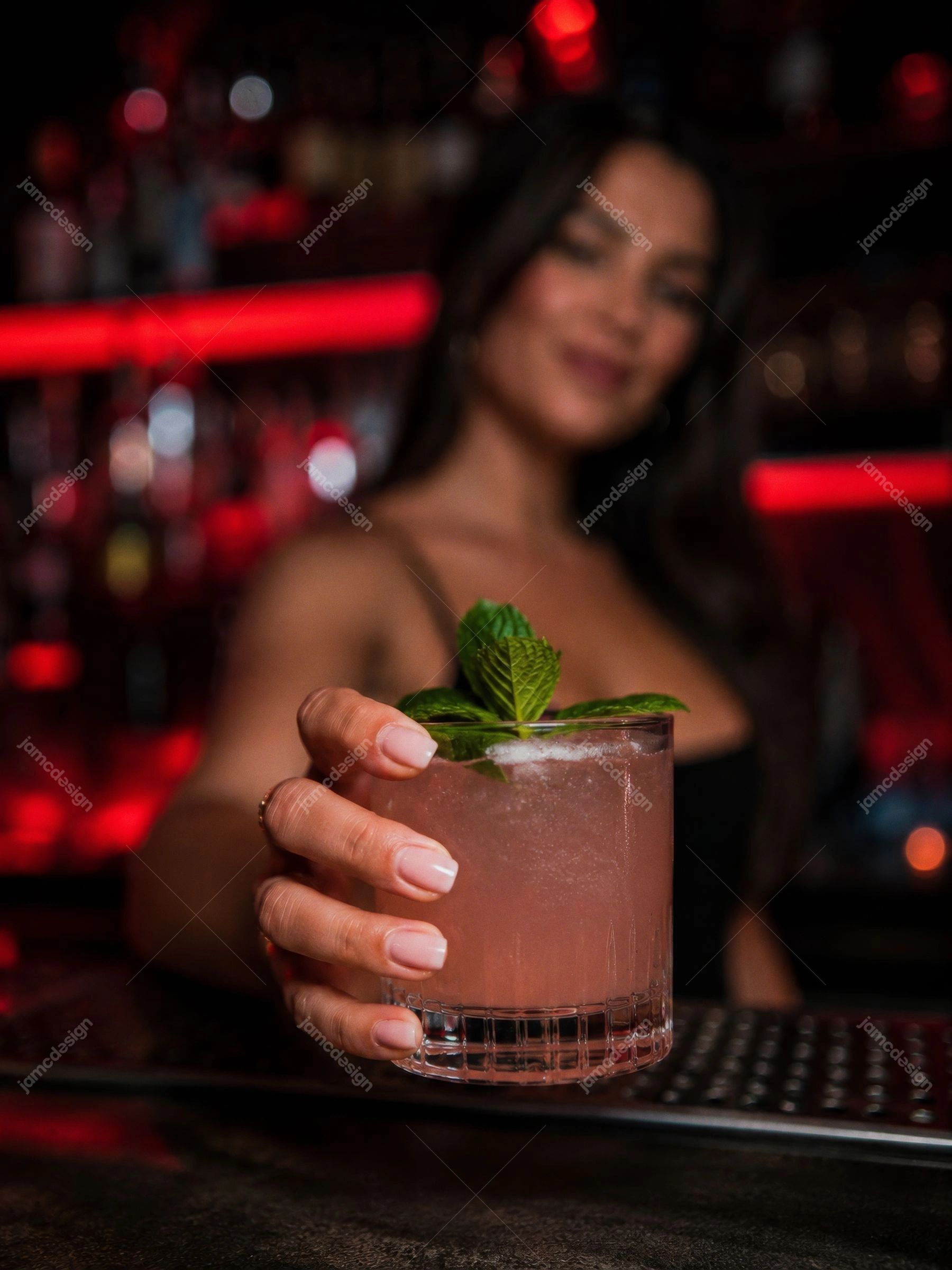 Bartender Oferecendo Coquetel Em Bar Com Luz Vermelha Com Bebida Rosa. Uma foto em JPG mostra uma bartender oferecendo um coquetel rosa decorado com hortelã