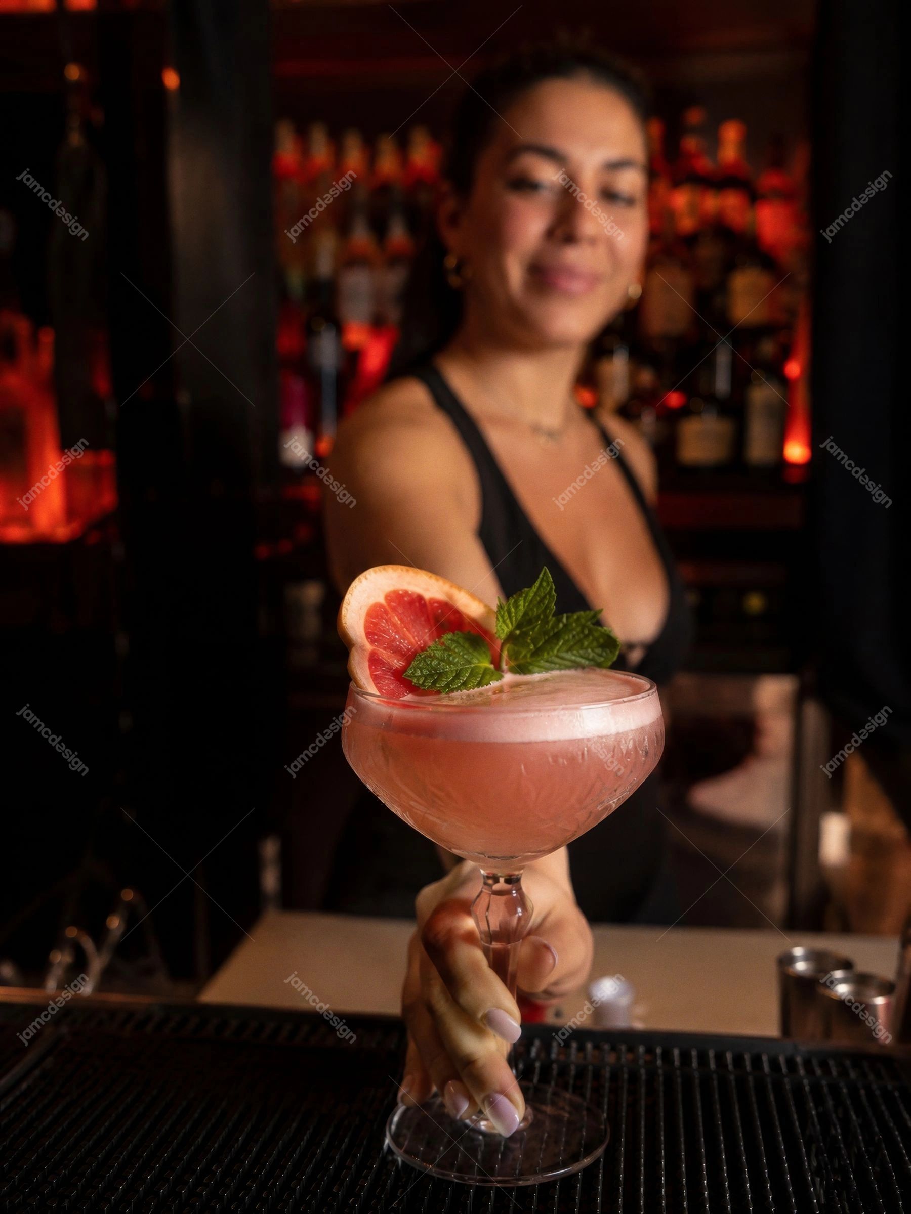 Bartender De Coquetel Rosa Com Hortelã Em Bar Noturno. Uma foto fotorrealista em JPG de um bartender servindo um coquetel rosa decorado com grapefruit