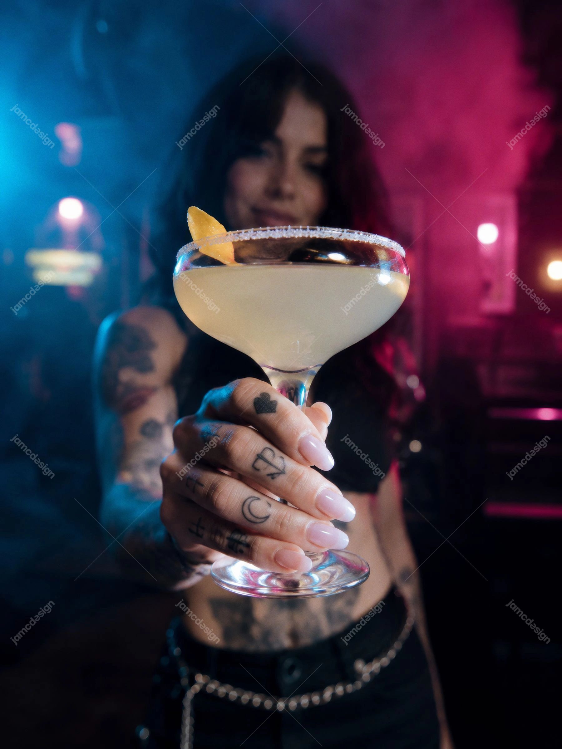 Coquetel Cítrico, Fumaça, Luzes Azuis De Clube E Coquetel Neon Azul. Foto JPG de um coquetel cítrico em uma taça coupe, segurado por uma mulher tatuada