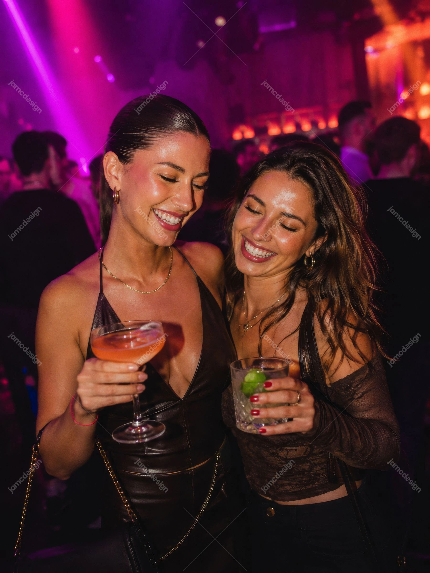 Foto De Duas Mulheres Brindando Com Coquetéis Na Boate. Foto em JPG de duas mulheres sorrindo e erguendo taças de coquetel dentro de uma boate movimentada